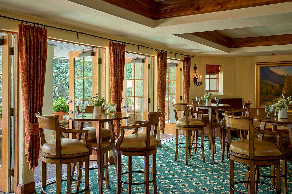 A cozy dining area with wooden chairs and tables, large windows, and warm lighting, perfect for relaxed meals and conversation.